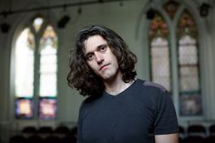 a man standing in front of a church with stained glass windows and long curly hair