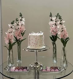 there are three vases with flowers and a cake on the glass table in front of it