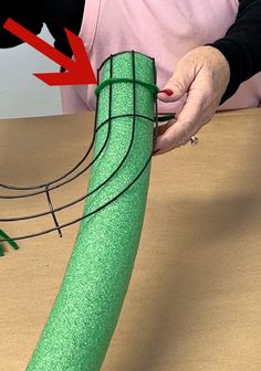 a person is making a green object out of paper and wire on a table with an arrow pointing to it