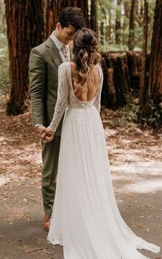 a bride and groom are standing in the woods holding each other's hands as they look at each other