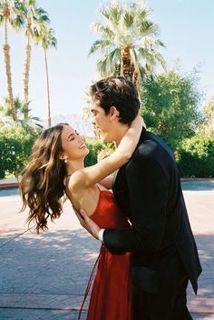 a man and woman in formal wear embracing each other with palm trees in the background