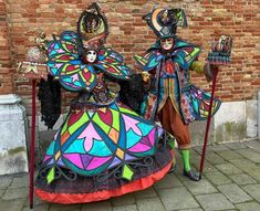 two people dressed in brightly colored costumes standing next to each other near a brick wall