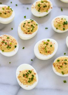 deviled eggs topped with chives and seasoning on a white marble countertop