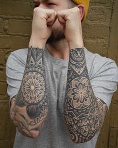 a man with tattoos on his arms covering his eyes