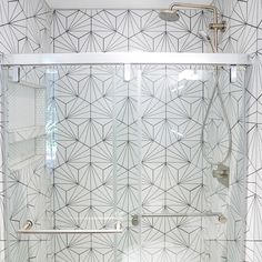 a bathroom with a glass shower door and white tile flooring, along with a black and white patterned wall