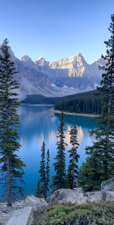 a lake surrounded by trees and mountains with snow on the mountain peaks in the distance