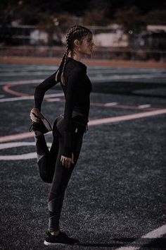 a woman standing on one leg with her hands behind her back, wearing a black wetsuit