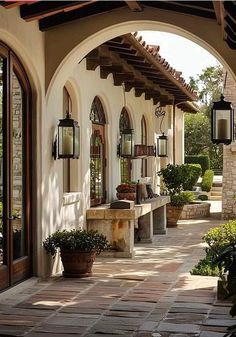 an arched walkway with potted plants and hanging lanterns on the side of the building