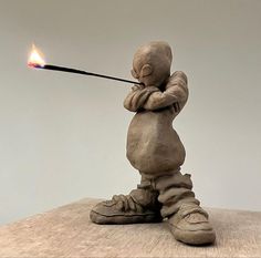 a clay sculpture holding a lit match in its hand and standing on top of a wooden table