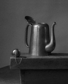 a metal teapot sitting on top of a wooden table next to a silver ball