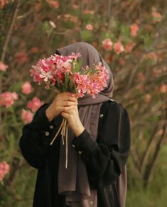 a woman wearing a hijab holding flowers in front of her face