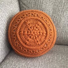 an orange crocheted round pillow sitting on the back of a gray couch cushion