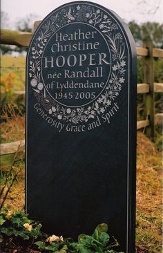 a grave marker in the middle of a grassy area with flowers around it and a wooden fence behind it