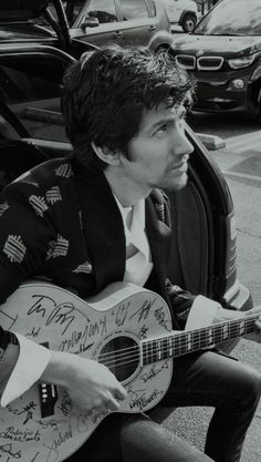 a man sitting on the ground with a guitar in his lap and autographed