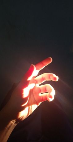 a person holding their hand out in the air with light shining on them and dark background