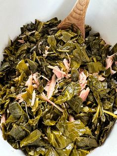 a white bowl filled with greens and meats next to a wooden spoon in it