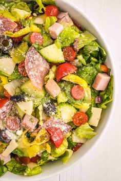 a salad with ham, lettuce and tomatoes in a white bowl on a table