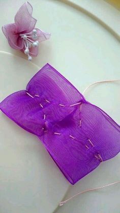 a purple piece of cloth with some thread on it next to a small pink flower