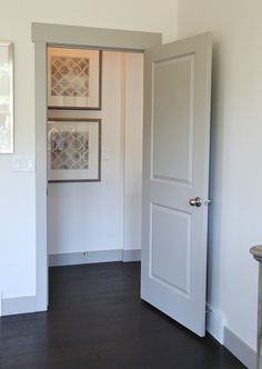 an open door in a white room with wood flooring and wall art on the walls