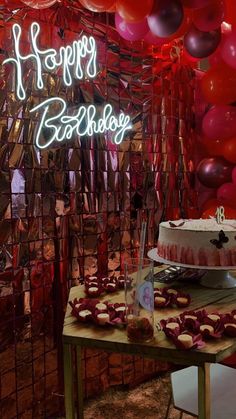 a birthday cake and cupcakes on a table in front of balloons with the words happy birthday