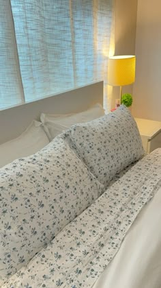 a white bed with blue flowers on it and a yellow lamp next to the headboard