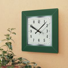 a green square clock mounted to the side of a wall next to a potted plant