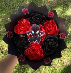 a bouquet of red and black roses in someone's hand on the grass with spiderman stickers