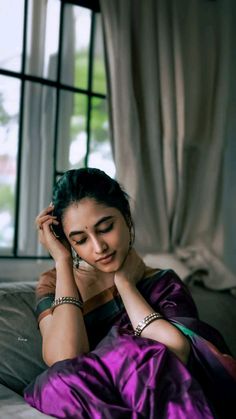 a woman sitting on top of a bed talking on a cell phone with her hand near her ear