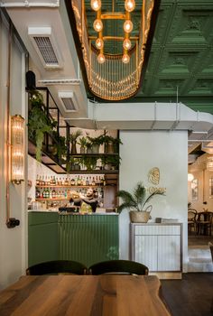 the interior of a restaurant with wooden tables and green chairs, hanging lights and potted plants