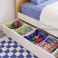 an open drawer with toys in it on a blue and white checkered rug next to a bed