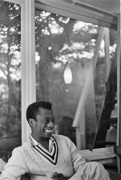 a black and white photo of a smiling man sitting in front of a large window