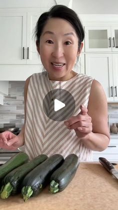 a woman standing in front of cucumbers on a kitchen counter with a knife