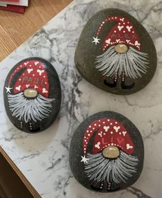 three painted rocks with santa hats on them sitting on a marble counter top next to a red and white envelope