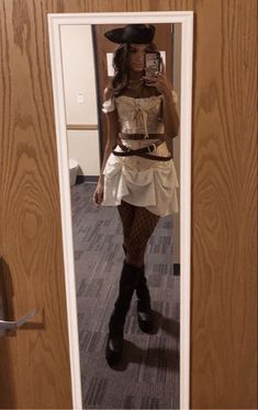 a woman taking a selfie in a mirror wearing a cowboy hat and white dress