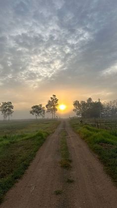 the sun is setting over a dirt road