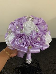 a bridal bouquet in purple and white with pearls on the top is being held by a woman's hand