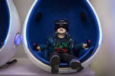 a young boy sitting in a blue chair with virtual glasses on his head and looking at the camera