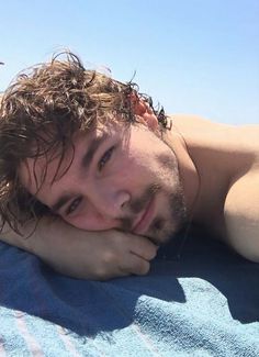 a man laying on top of a blue towel next to the ocean with his hand under his chin