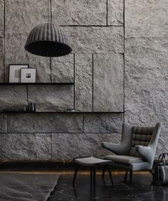 an empty chair and ottoman in front of a stone wall with a lamp above it