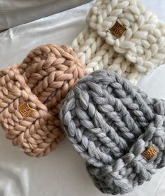 three knitted beanies sitting on top of a white bed next to each other