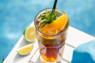 a glass filled with liquid next to lemons and lime slices on a white tray