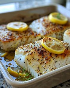 some fish with lemon slices and seasoning in a white dish on a counter top