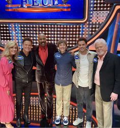 five people posing for a photo in front of a tv set with the caption's name on it