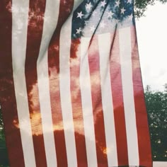 an american flag is waving in the wind with trees in the background