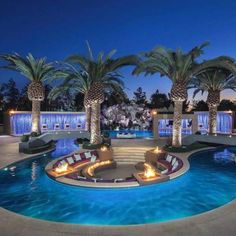 an outdoor swimming pool with lounge chairs and palm trees in the background at night time