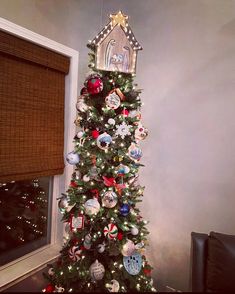 a christmas tree with ornaments and a church on it's top, in front of a window