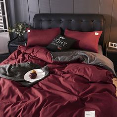 a bed with a red comforter and pillows on it, next to a black headboard