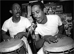 two men sitting next to each other playing drums