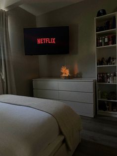 a bedroom with a television mounted on the wall next to a bed and dresser in front of it