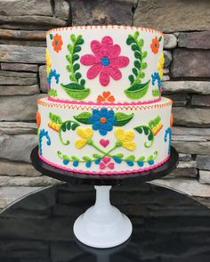 a multi - colored decorated cake sitting on top of a black table next to a stone wall